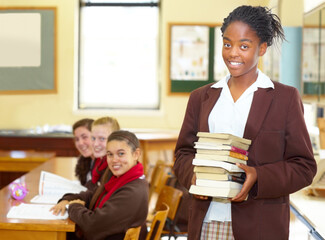 Shes an A-student. Smiling young high school student holding books while standing in the classroom.