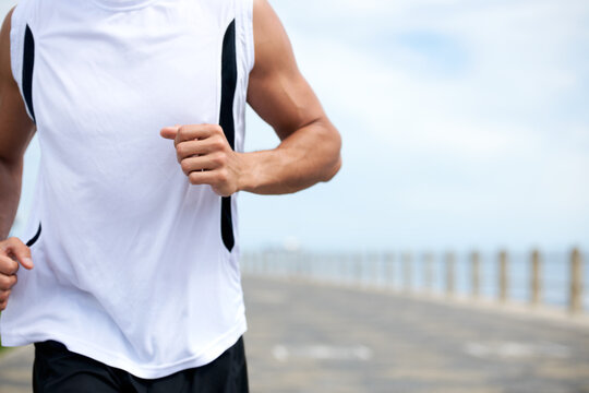 Push your body beyond its limits. Cropped image of a fit and athletic male running on a beach promenade outside - copyspace.