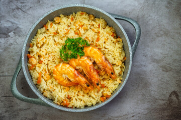Rice with shrimps in a frying pan on a wooden table, top view.