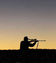 Fototapeta na wymiar Preparing to shoot. A silhouette of a man in the outdoors holding up his sniper rifle.