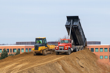 A large yellow dump truck unloads the sand