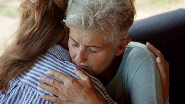 Adult daughter consoling unhappy senior mother and supporting her in struggle indoors at home.