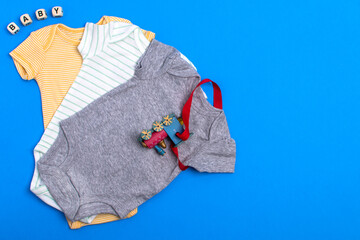 yellow bodysuit, gray bodysuit and green cotton bodysuit with children's toy and blocks. Clothes for newborns on a blue background. Flat lay, top view.