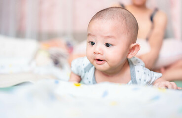 Happy family, Cute Asian newborn baby lying play on bed looking at something. While your mother takes care with love nearby. Innocent little boy on the first day of his life. Mother's Day concept.