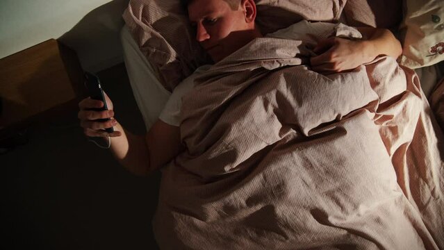Top shot Young Male Is using his phone in bed. Social Media addiction. Depressed