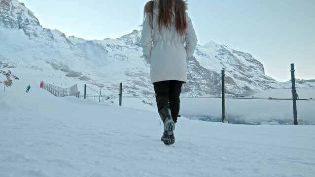 A fashionable girl in a winter jacket walking by The north face of the Eiger. A woman walks in slow motion in the winter in the Swiss Alps in  Kleine Scheidegg, Jungfrau Region, Switzerland.