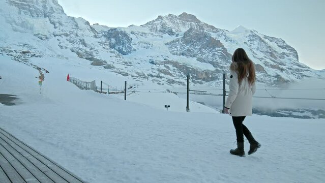A fashionable girl in a winter jacket walking by The north face of the Eiger. A woman walks in slow motion in the winter in the Swiss Alps in  Kleine Scheidegg, Jungfrau Region, Switzerland.