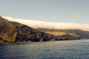 Fog rolls over the northern edge of Guadalupe Islland off Bsjs Mexico coast. Note; Large sportfishing boat near island