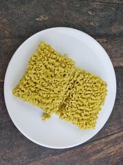 Dry yellow noodles on a white plate on a wooden background
