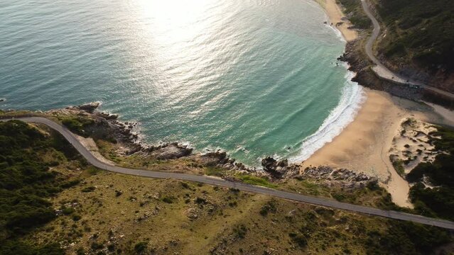 Coastal landscape with beach and road, sun rays reflecting in sea. Aerial circling