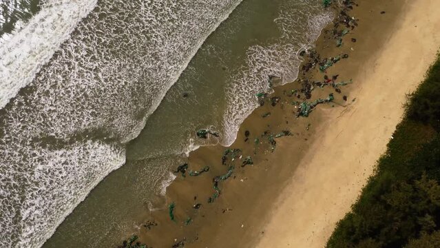 Ocean pollution, Aerial top down view of ocean waves crashing on tropical sandy beach paradise polluted with plastic fisherman net in Vietnam 