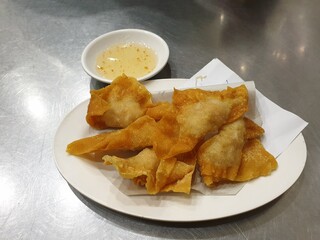 Fried dumplings stuffed with minced pork in a white plate with a cup of white plum sauce placed on the silver table