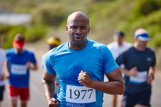 Feeling strong and invincible on the road. Shot of a young man running a marathon with other runners in the background.