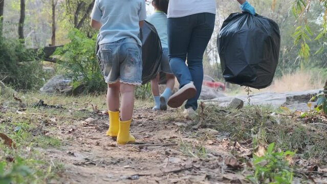 Group of Asian volunteer families tying a garbage bag and carry it out after picking up trash by the river. Put garbage in the bin to help save the environment. World Environment Day
