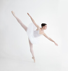 Obraz premium Balance is crucial. Elegant young ballerina dancing en pointe against a white background in penche position.