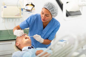 Focused woman dentist working in the clinic treats a man patient who is sitting in a dental chair...