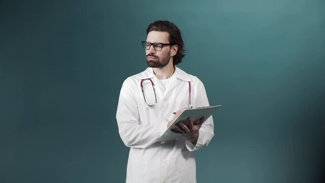 A young doctor in a white gown is writing something down on a tablet keeping in his hands