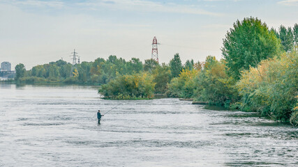 A fisherman standing in the water against the background of bushes
