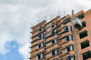 Fototapeta premium Bottom view of a building under construction with scaffolding against the sky