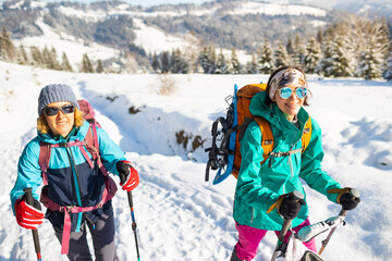 Two women walk with snowshoes on the backpacks, winter trekking