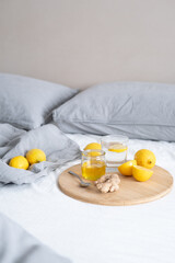 A Glass of water on a wooden serving tray with ginger root, honey and a slice of lemon on a on bed. High quality photo