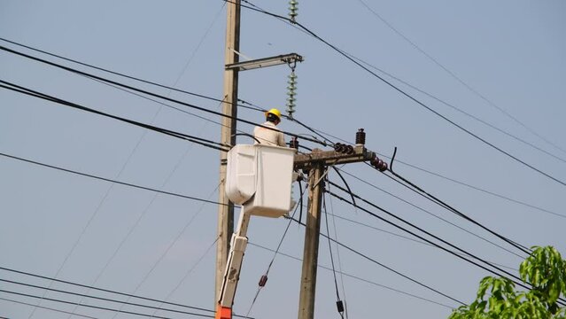 Electrician worker in lift bucket working on an electric pole to install and repair wires.