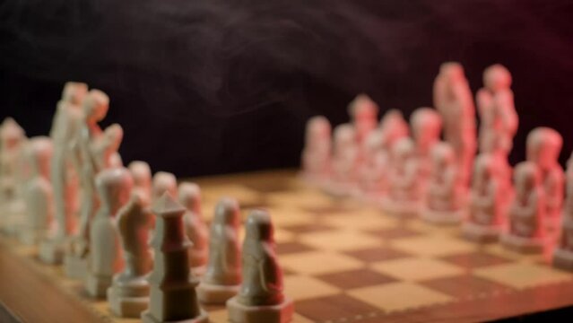 A close up dolly shot tracking in towards the chequered squares of a wooden chessboard, the pieces are placed ready and set the scene for a new chess match to begin 