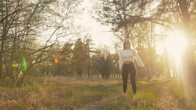 Attractive young woman in sweater, jeans is dance and spinning among blossom apple tree. Sunset, spring orchard and green field. Slow motion. Caucasian one girl, long fluttering hair. Sun glasses.
