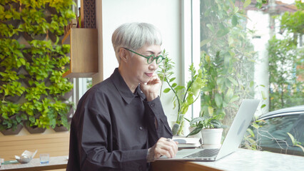 An old elderly Asian retired senior woman using a computer laptop notebook device in coffee shop or restaurant. People on social media internet technology. Technology lifestyle