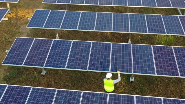 Aerial drone view, Flight over solar panel farm, young engineer talking on smartphone while checking on operation of sun and cleanliness of photovoltaic solar panels at sunset