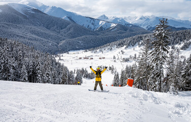 Beautiful landscape of the Arkhyz ski resort with mountains, snow, forest and man snowboarder in yellow jacket and backpack on a sunny winter day.  Caucasus  Mountains, Russia