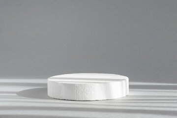 Geometric white podium. Round 3d shape, for demonstrating beauty products on a gray background in rays of sunlight