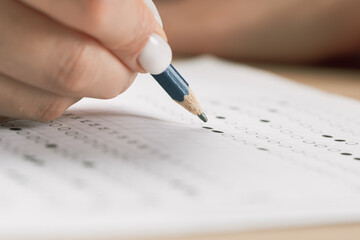 student hand testing in exercise and passing exam carbon paper computer sheet with pencil in school test room, education concept