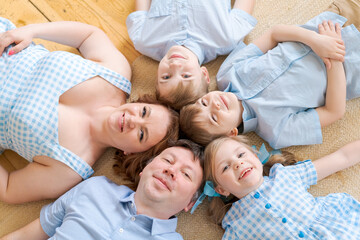 Fototapeta na wymiar Portrait happy caucasian family posing on floor house, lying on carpet and approaching, smiling cheerfully, top view. Positive european father, mother and daughter and two brothers hugging