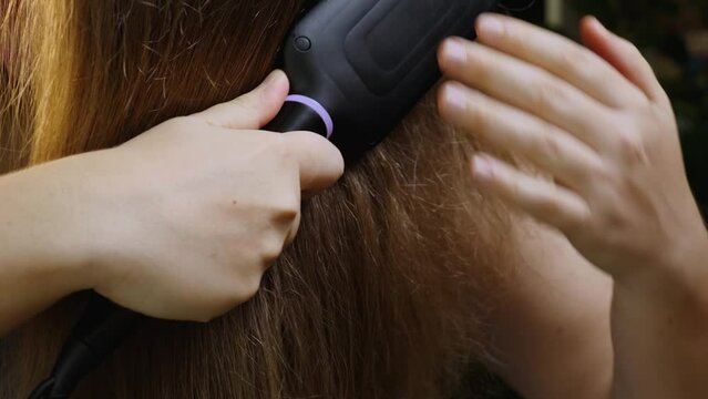Close-up of a girl in a blue towel brushing her hair with a special electric straightening brush. Heated, ceramic, non-damaging hair brush. Front view. Hair care