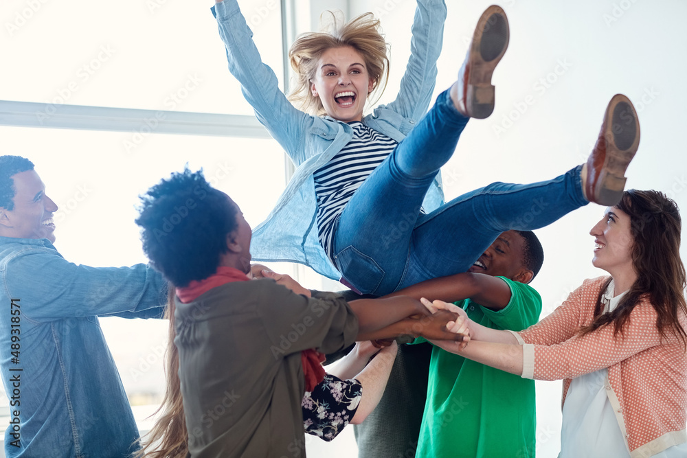 Poster getting crazy on campus. shot of a group of university students tossing another student in their air