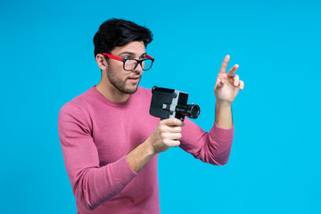 Caucasian Brunet Man in Pink Coral Jumper And Hipster Glasses While Holding Retro Film Camera in Hands Against Blue Background.