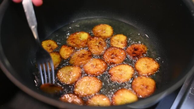 Removing plantains cooking in coconut oil with a fork from a frying pan, handheld