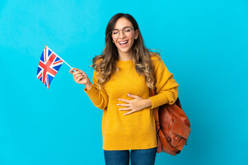 Young hispanic woman holding an United Kingdom flag isolated on blue background smiling a lot