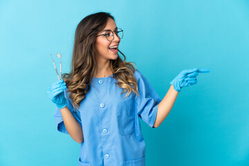 Woman dentist holding tools over isolated on blue background pointing finger to the side and presenting a product
