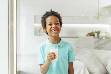 Laughing kid boy drinking milk at home
