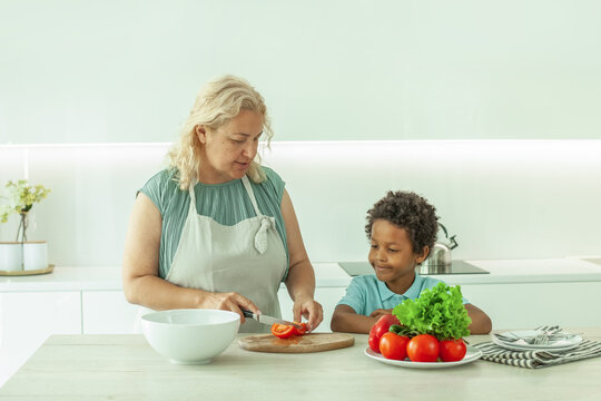 Kid boy and matre woman preparing food in white kitchen background