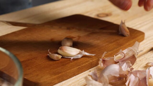 Close-up of a woman's hands crushing garlic cloves on a cutting board with a large knife. A simple and convenient way to peel garlic from the husks. Healthy and wholesome food every day