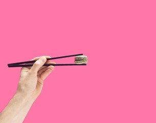 Minimal asia artisan food concept. The man's hand holding black chopsticks with green yummy macaron. Bright pink background