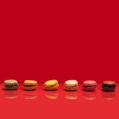 Sixt different color and taste macarons in a horizontal line against a smooth red background. Creative copy space above.