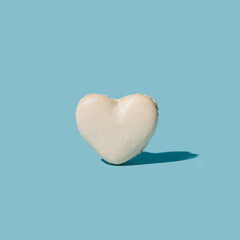 French patisserie minimal artisan concept. White heart shaped attractive macaron alone against pastel blue background