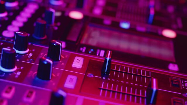 Hand of professional DJ adjusts cue slider on fader in digital music console in neon light nightclub, closeup. Concept professional musical accompaniment of party