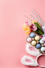 easter background with eggs, bunny ears and tulips on pink backdrop, top view flat lay
