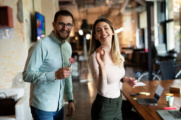 Young colleagues taking break after work. Happy young businessman and businesswoman playing darts in the office.