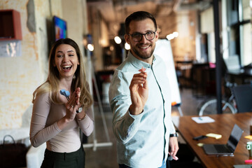 Young colleagues taking break after work. Happy young businessman and businesswoman playing darts in the office.